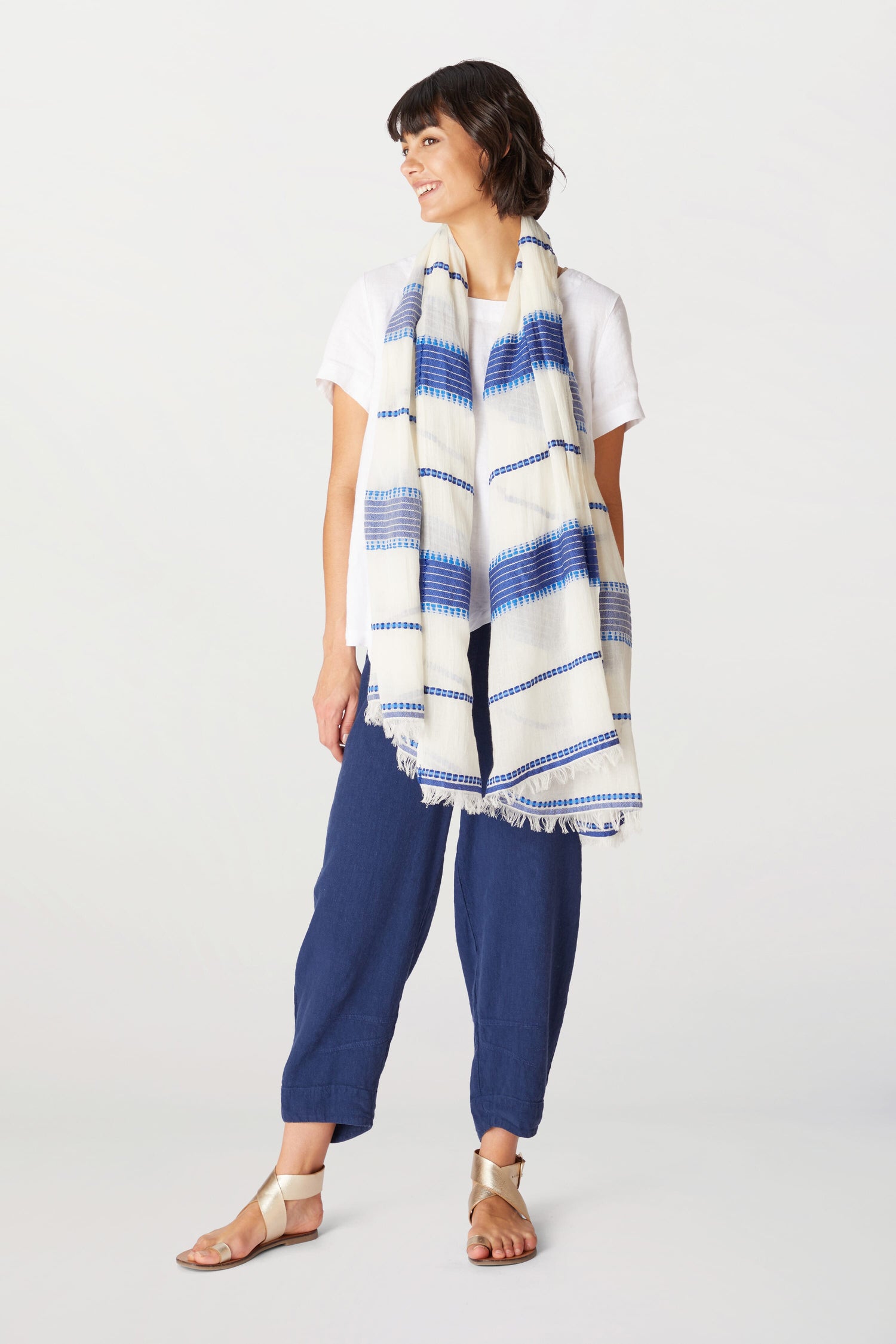 Woman in a white t-shirt and blue pants, standing with one hand on her hip, wearing an Embroidered Stripe Scarf and sandals.