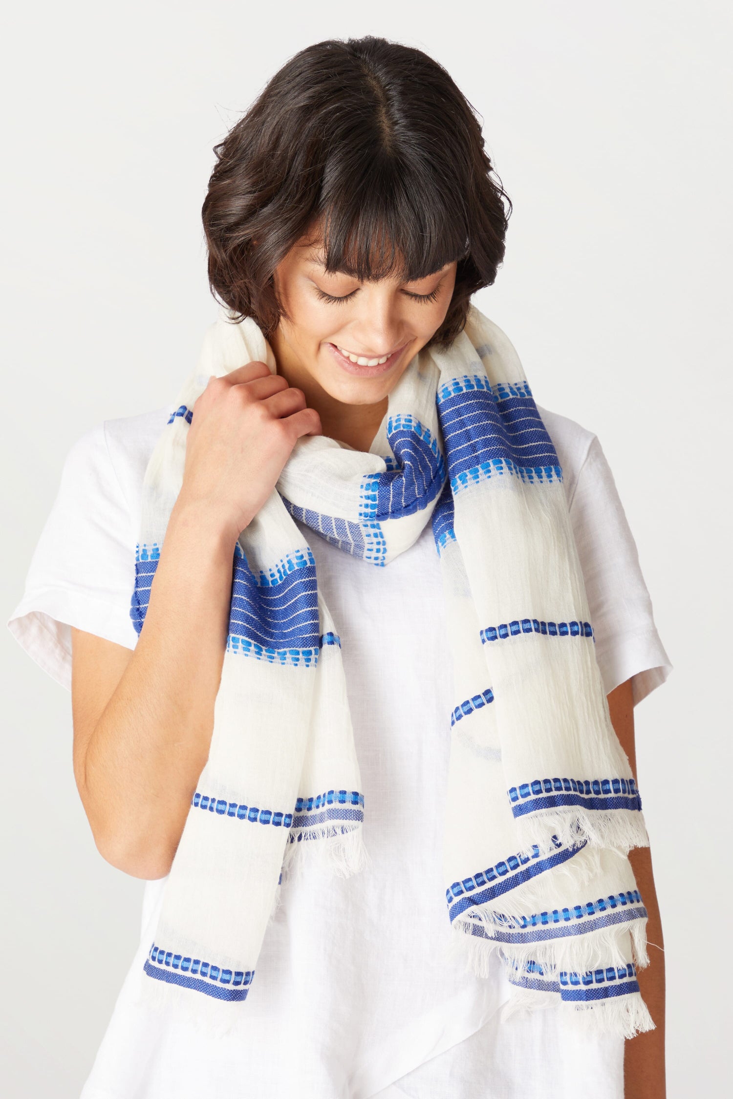 Woman in white shirt smiling slightly while holding a Embroidered Stripe Scarf around her neck.