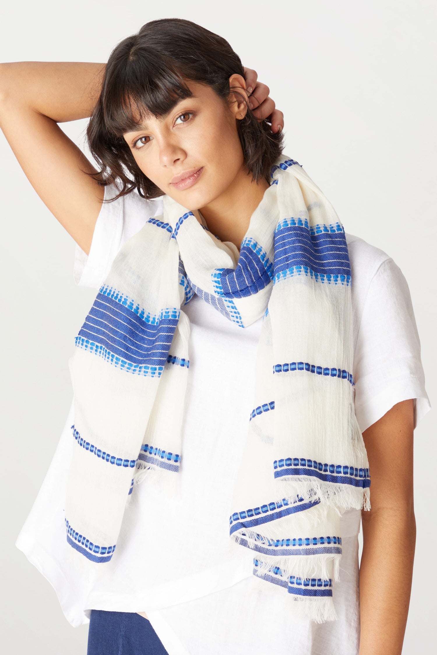 A woman with a bob haircut wearing a white t-shirt and an Embroidered Stripe Scarf poses with her hand in her hair.