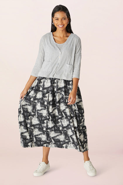 Woman smiling, wearing a Stripe Button Cardi, white top, and a monochrome patterned midi skirt, paired with white sneakers.