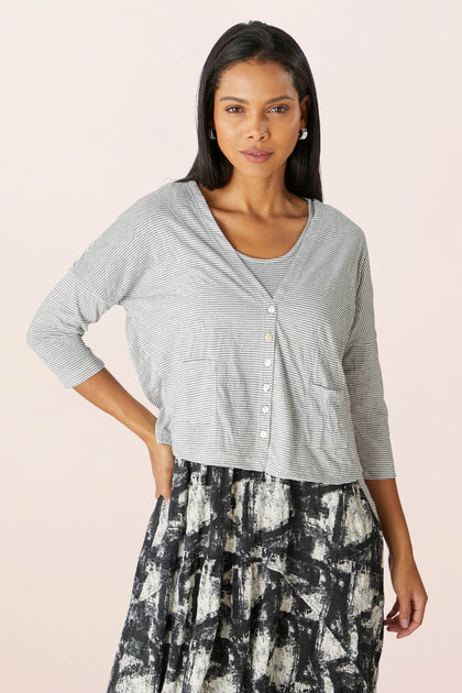 A woman in a gray Stripe Button Cardi and a black and white abstract skirt standing against a pink background.