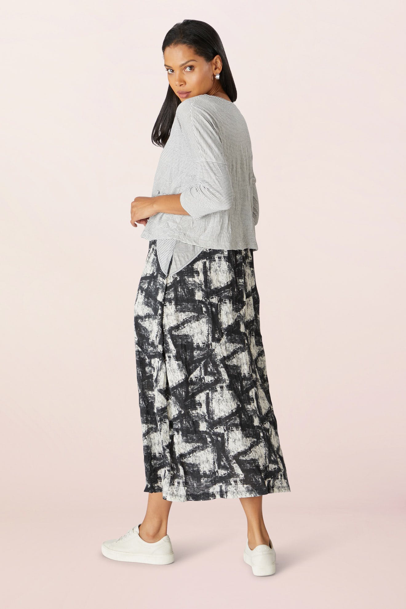 A woman wearing a Stripe Button Cardi, black and white patterned skirt, and white sneakers stands facing away, glancing over her shoulder.