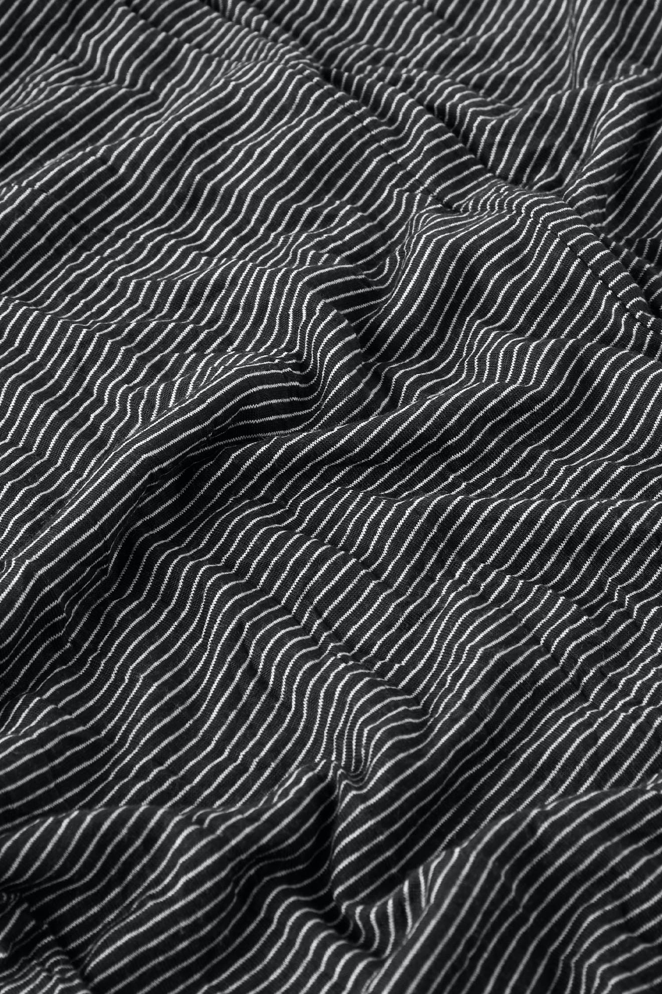 Close-up of a textured, crinkled jersey knit fabric with a wavy, striped black and white Stripe Pant pattern.