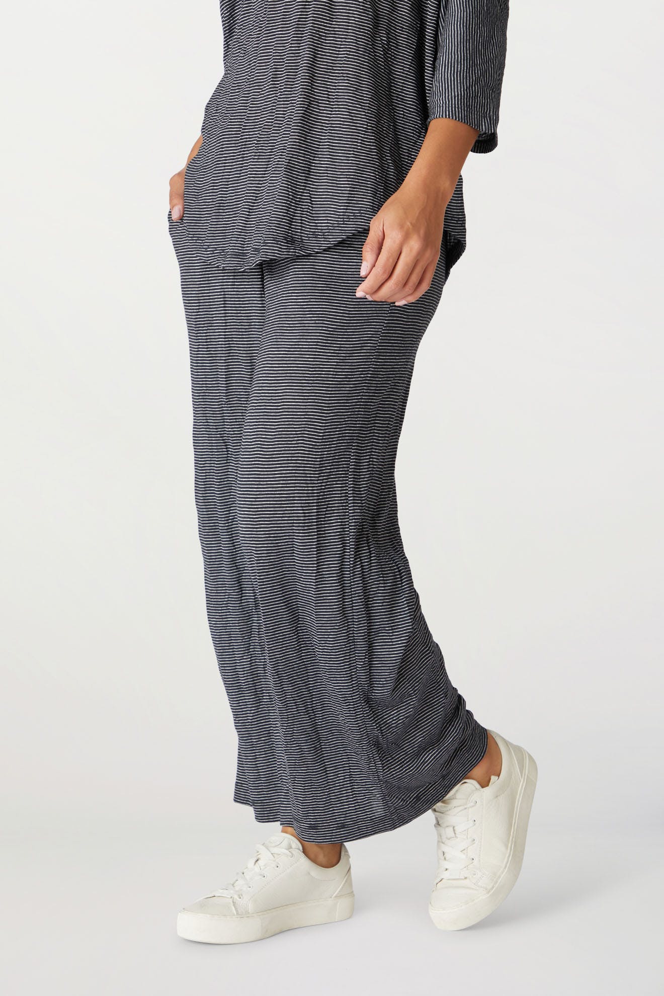 Woman in crinkled jersey knit, grey striped outfit with Stripe Pant and a long top, paired with white sneakers, shown from the waist down.
