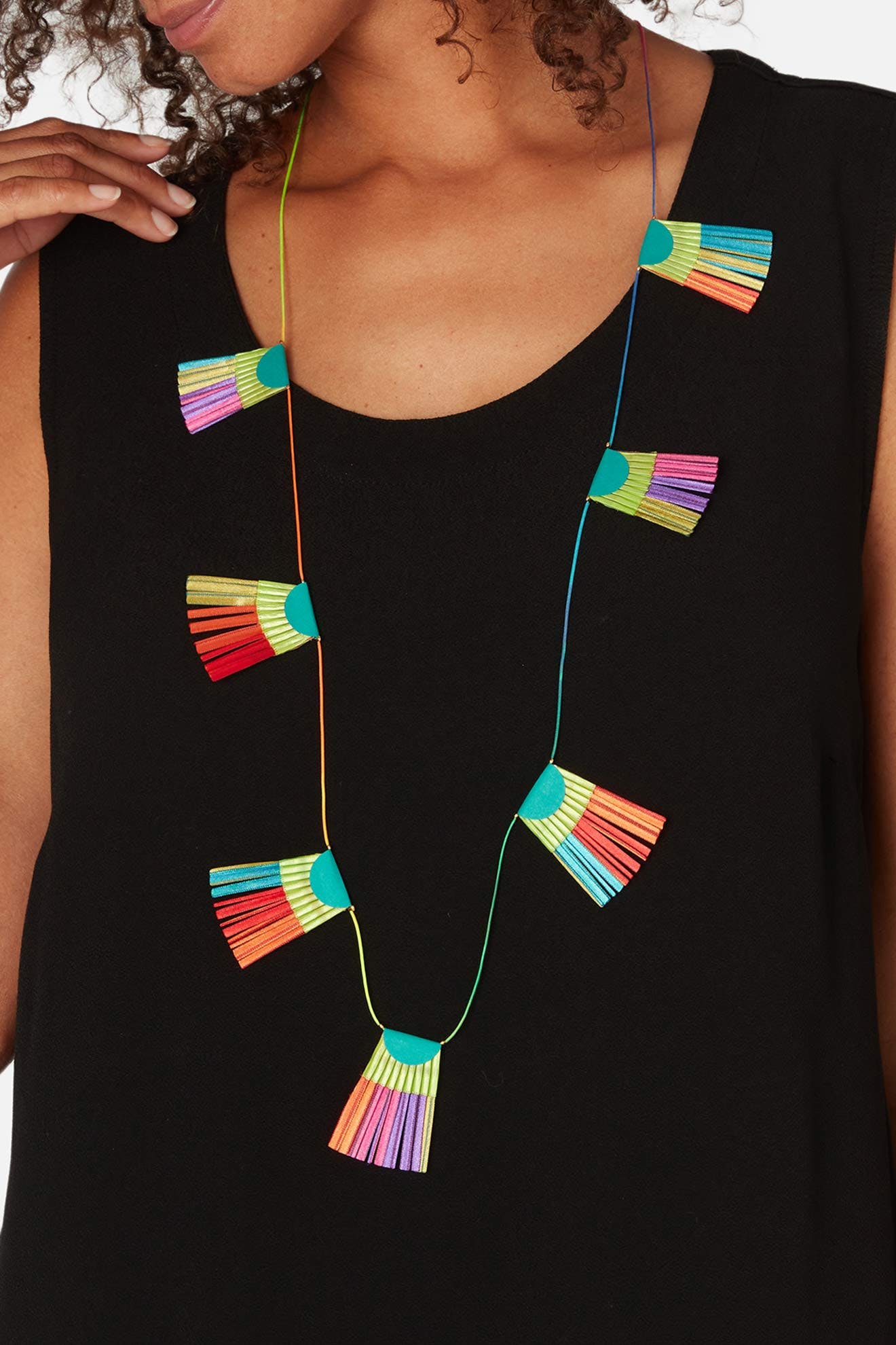 A person wearing a black top features the vibrant Fan Detail Necklace by Alexandra Tsoukala, adorned with hanging tassels in bright shades of blue, red, green, yellow, and purple.