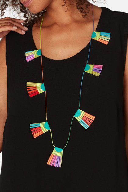 A person wearing a black top features the vibrant Fan Detail Necklace by Alexandra Tsoukala, adorned with hanging tassels in bright shades of blue, red, green, yellow, and purple.