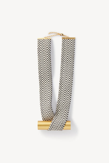 Gold and black chevron patterned scarf draped over a cylindrical holder featuring the Balance Necklace by Christina Brampti against a white background.