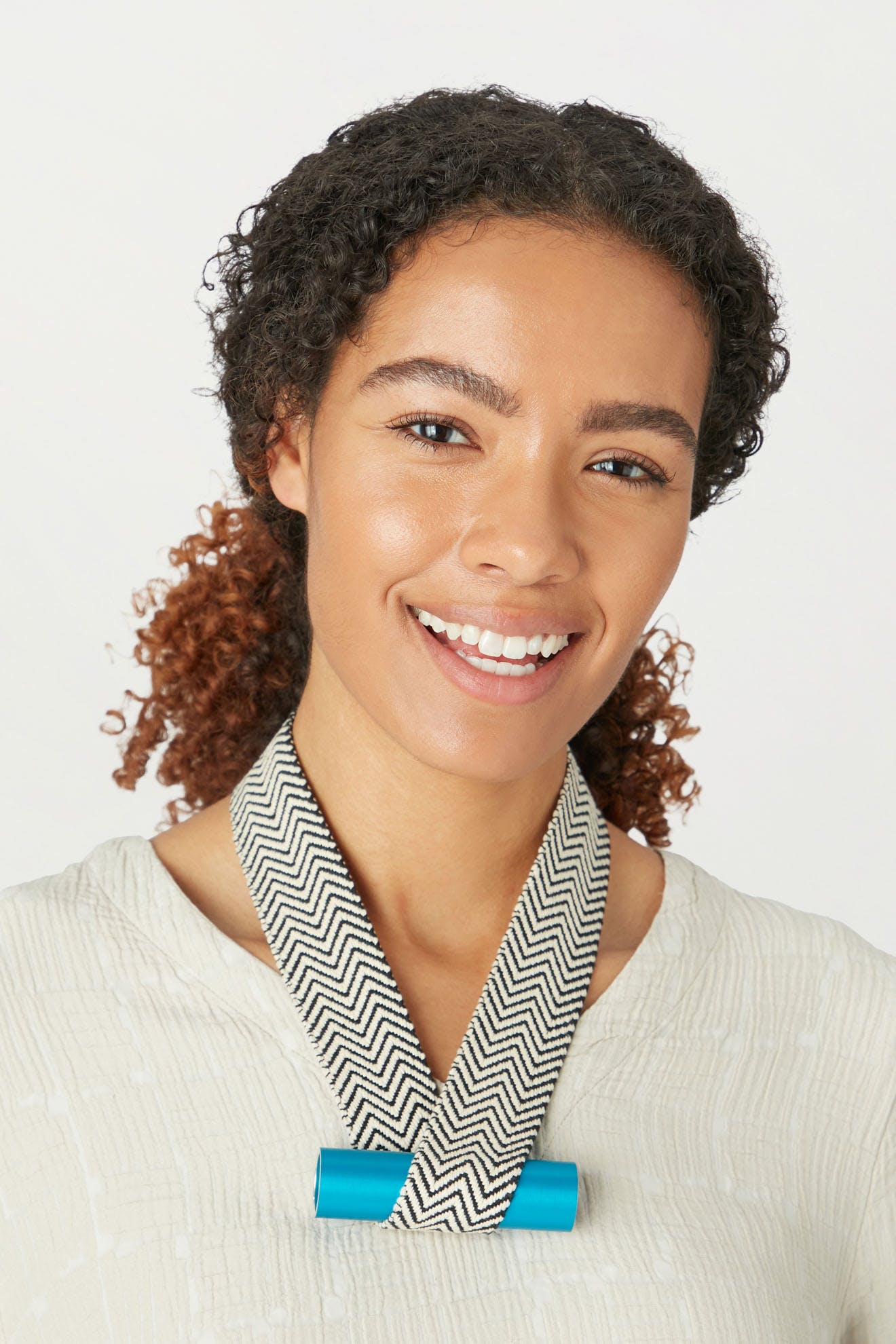 Woman with curly hair smiling at the camera, wearing a white blouse with a chevron-patterned collar and the Balance Necklace by Christina Brampti.