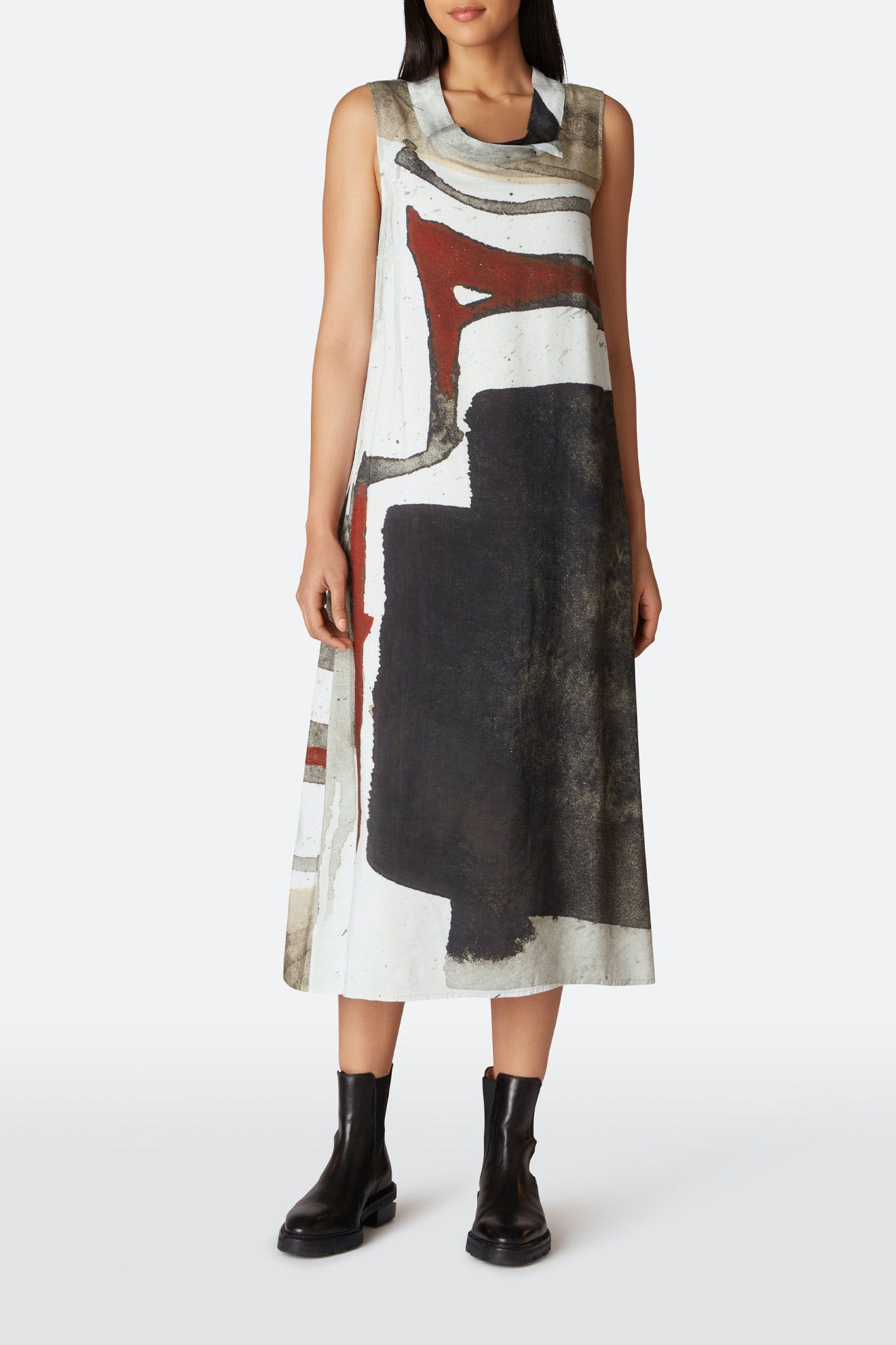Woman wearing a sleeveless, cowl print dress paired with black ankle boots, standing against a white background.