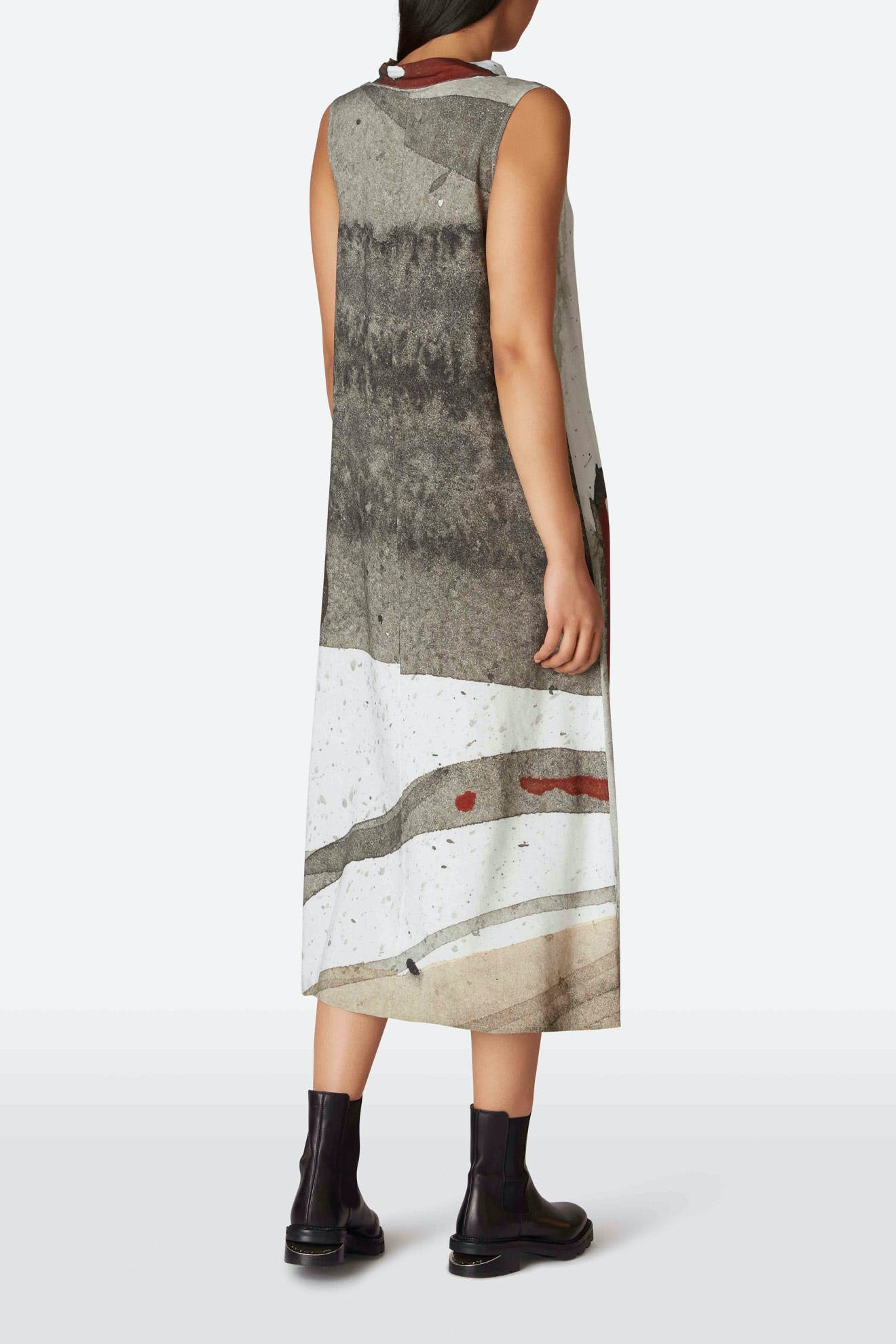 Rear view of a child wearing a sleeveless Cowl Print Dress with abstract gray and white print, paired with black boots.