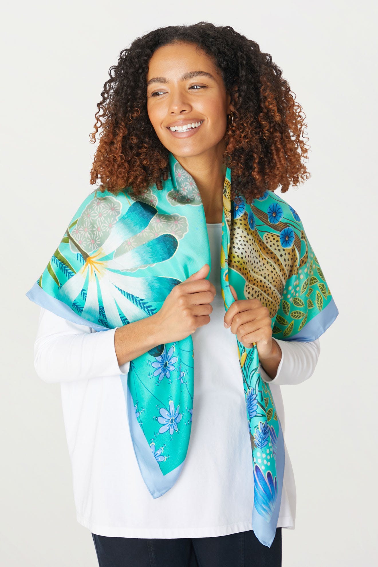 A woman wearing a blue and green tropical Moonlight Leopard Silk Scarf with vibrant prints.