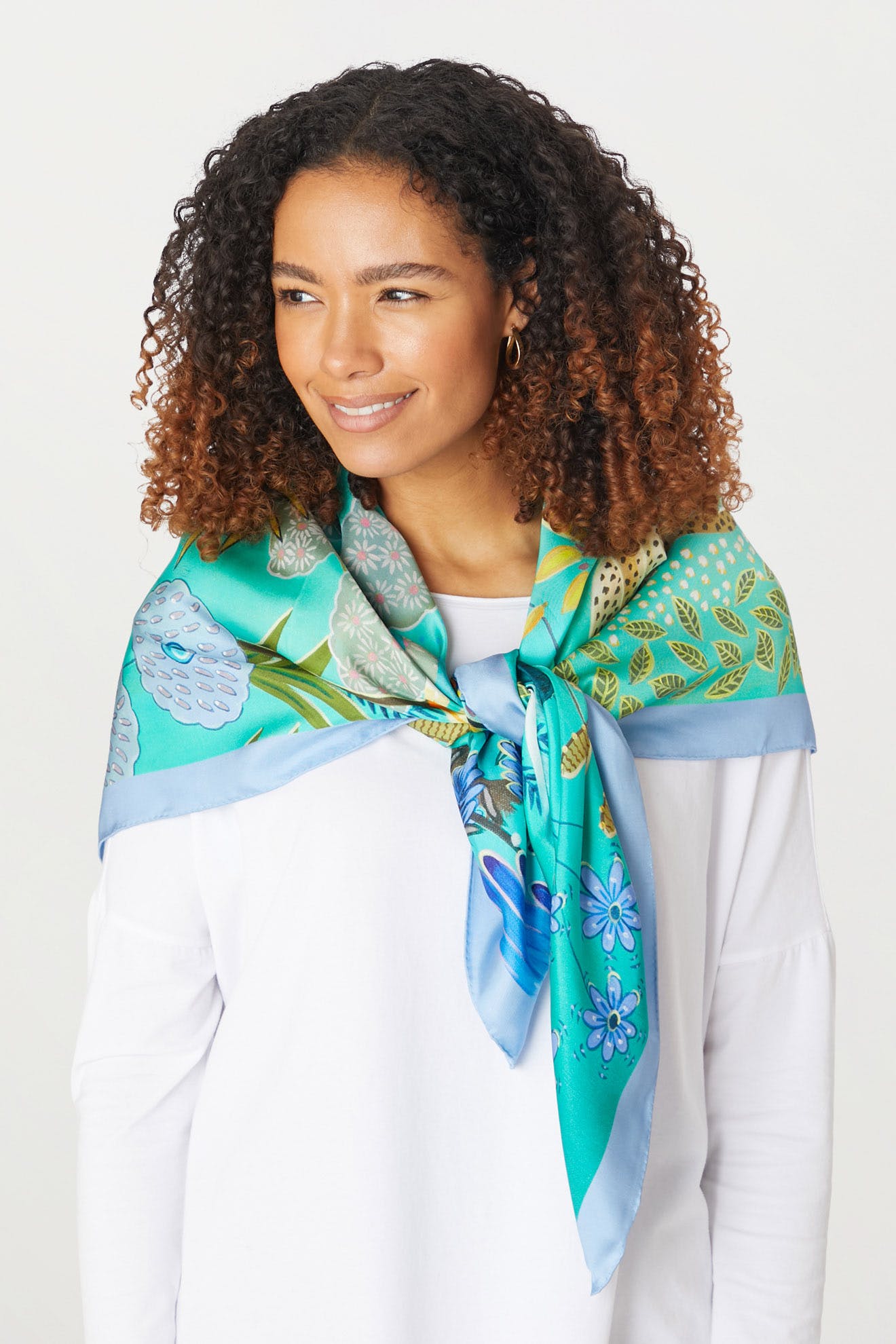 A young woman wearing a Moonlight Leopard Silk Scarf with green and blue prints of tropical scenes.