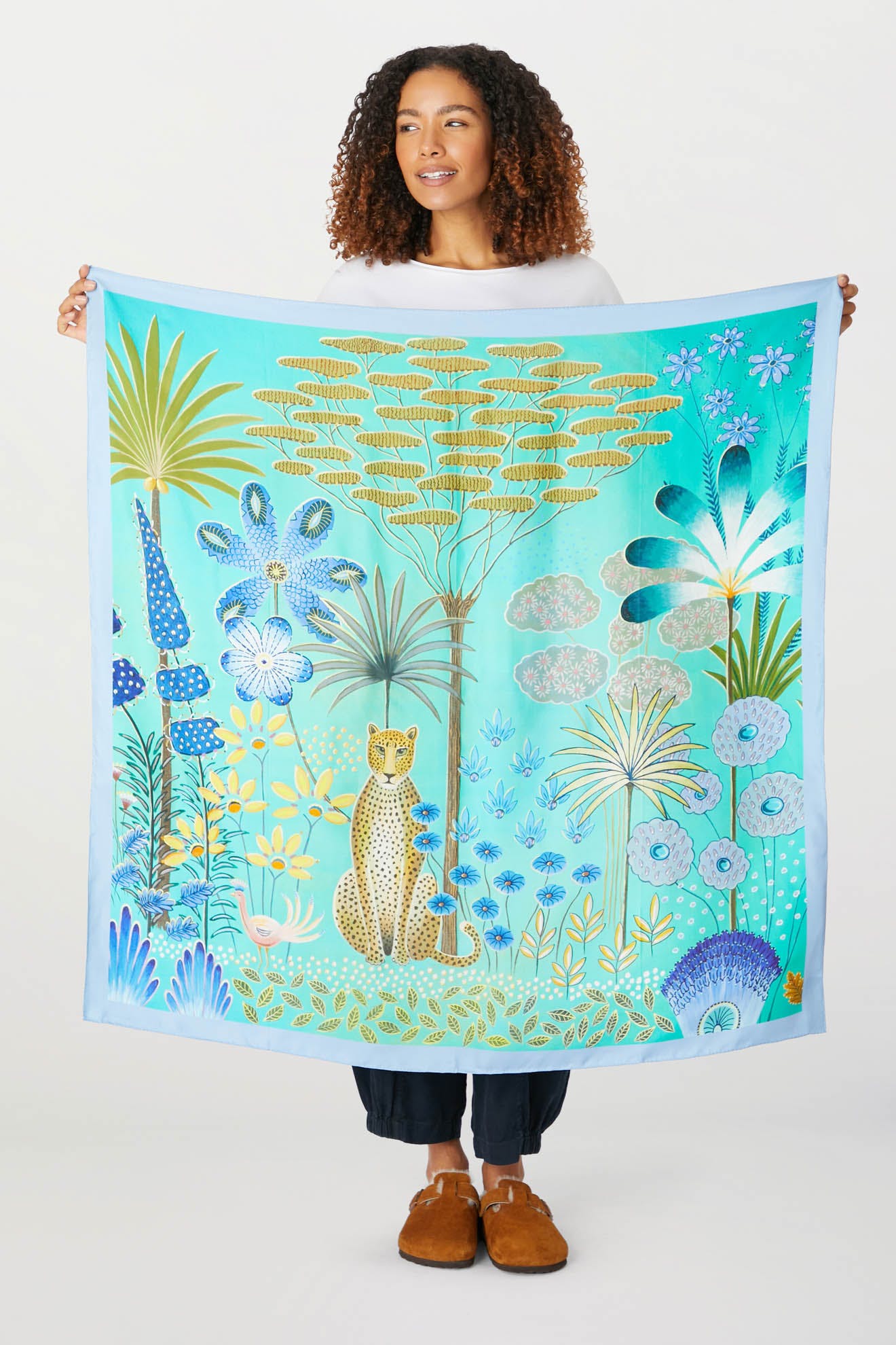 A woman is holding up a Moonlight Leopard Silk Scarf with a cat and flowers on it.