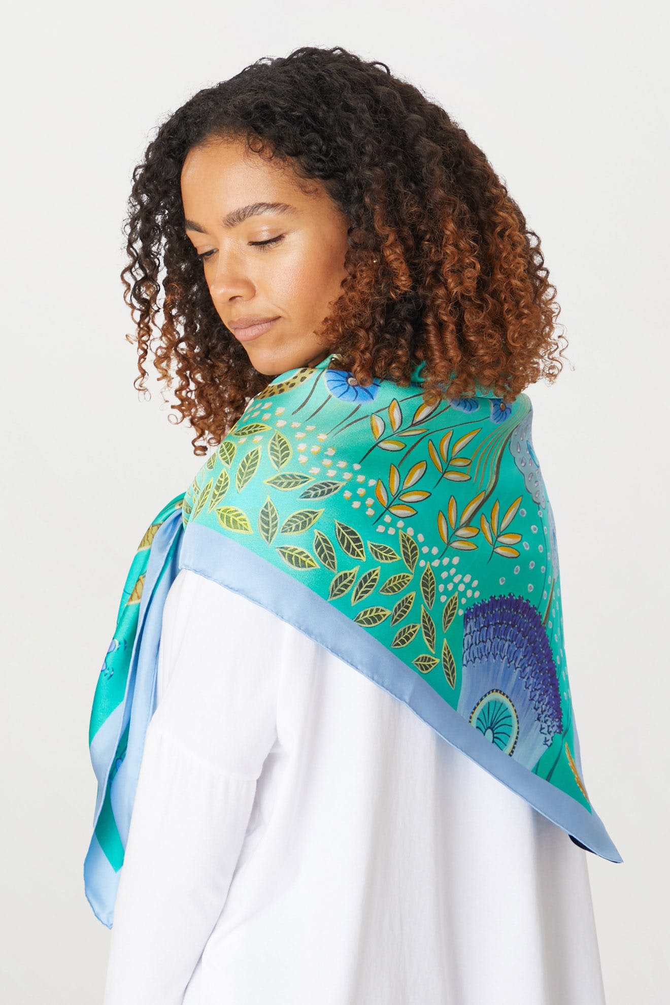 A woman wearing the Moonlight Leopard Silk Scarf with tropical scene prints in green and blue.