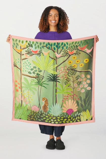 A woman is holding up an Are You Coming With Me Silk Scarf, showcasing the artist's stunning prints.