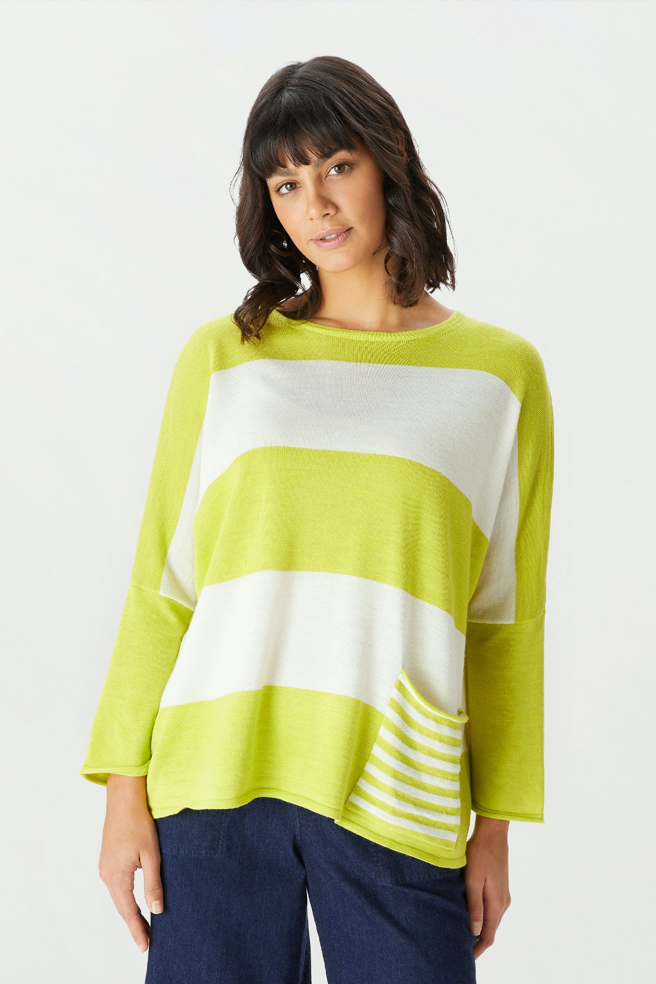 Wearing the Merino Blend Stripe Sweater—a loose-fit, long-sleeve lime green and white striped top featuring a striped pocket—paired with navy blue pants against a plain light background; an ideal outfit for transitional weather.