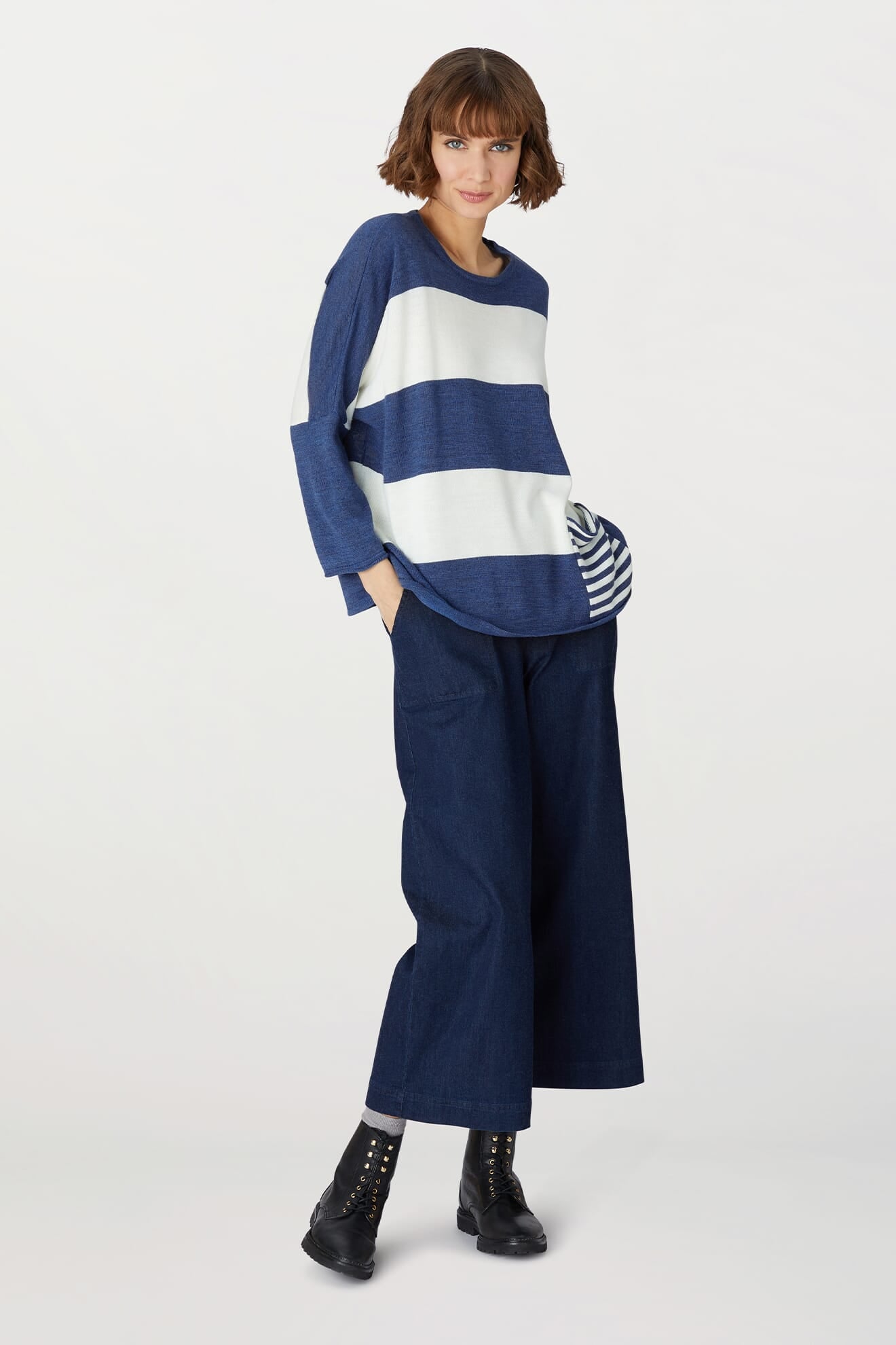 A woman wearing the Merino Blend Stripe Sweater in blue and white, paired with wide-leg dark blue jeans and black ankle boots, stands against a plain white background—a perfect look for transitional weather.
