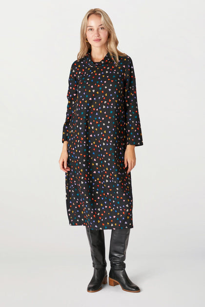 A woman in a Little Graphic Triangle Dress with colorful triangle prints, paired with black knee-high boots, posing against a white background.