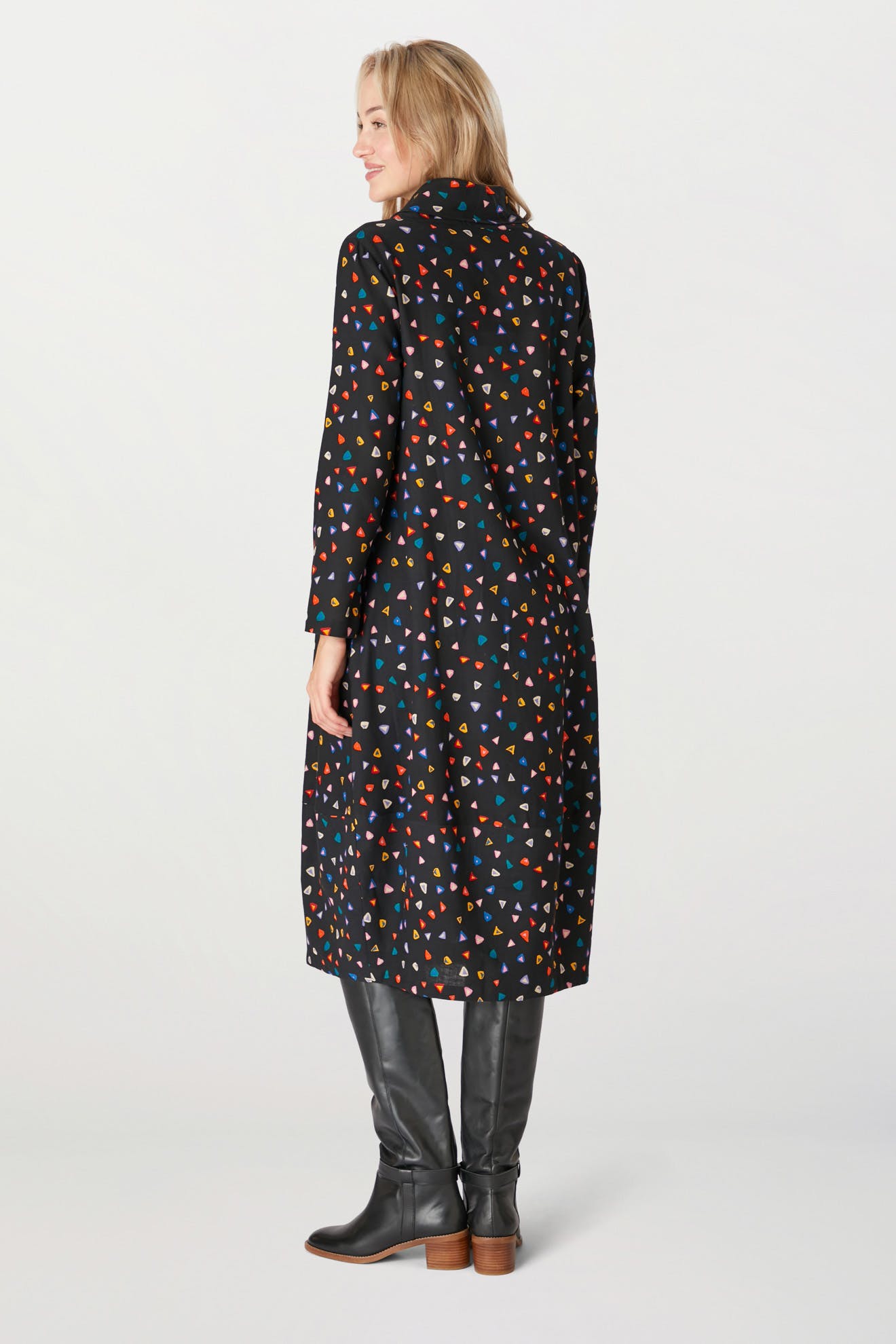 Woman in a black coat with a Little Graphic Triangle Dress, paired with knee-high boots, viewed from the back.
