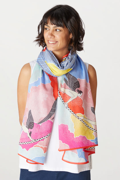 Woman with shoulder-length dark hair smiling, wearing a Yoga Flow Scarf with a unique sunrise-inspired print and a white sleeveless top.