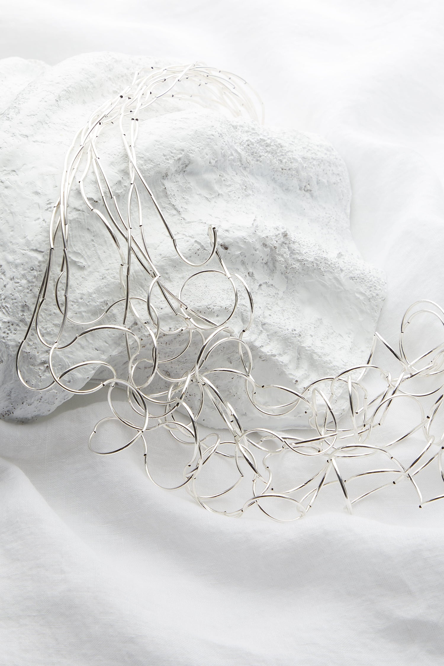 A Long Medley Necklace with an adjustable silver chain, laying on top of a white sheet.