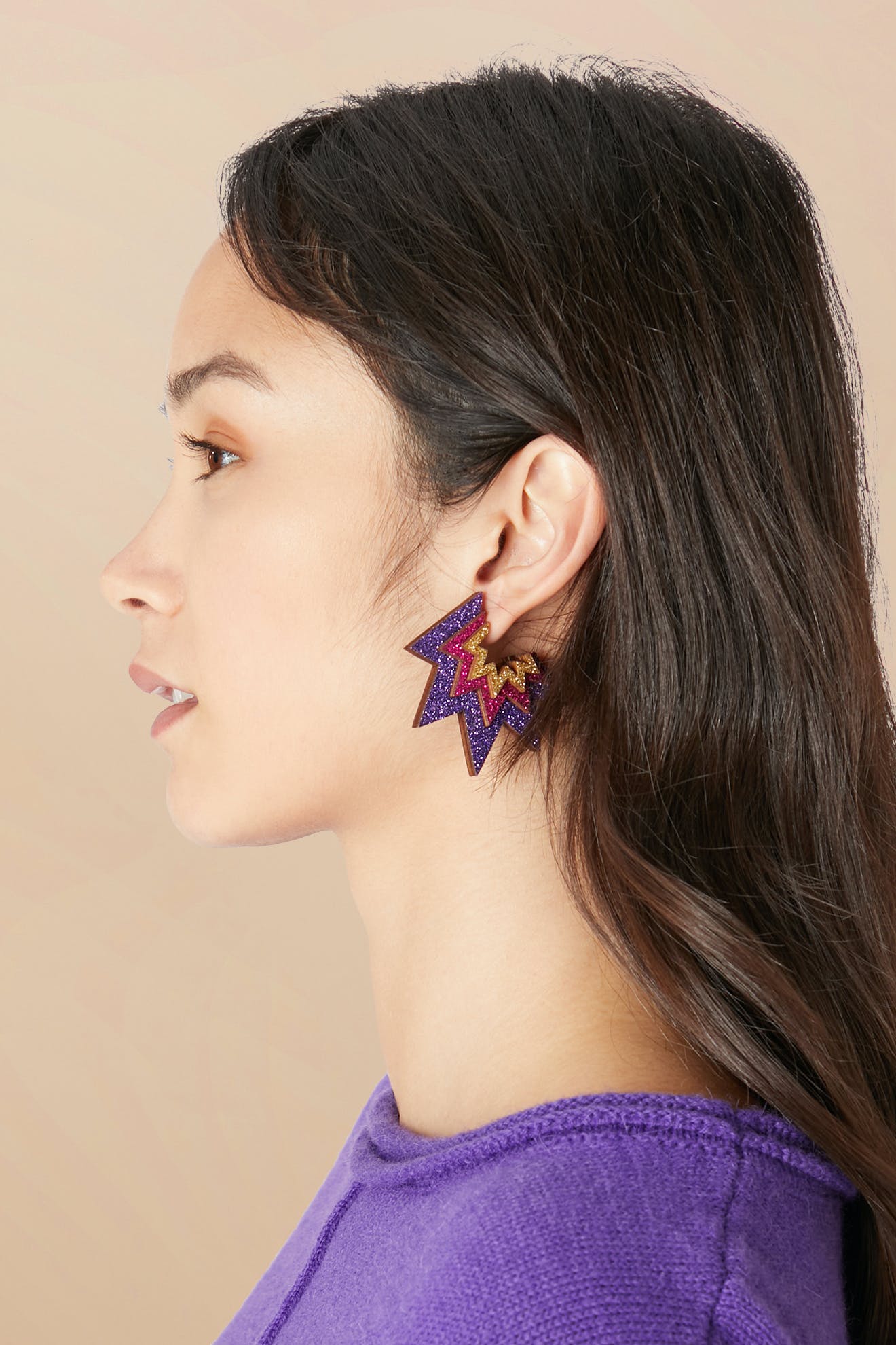 Profile view of a woman with long dark hair wearing a purple top and vibrant, zigzag-patterned Laser Cut Sparkle Hoops earrings crafted from eco-friendly wood.