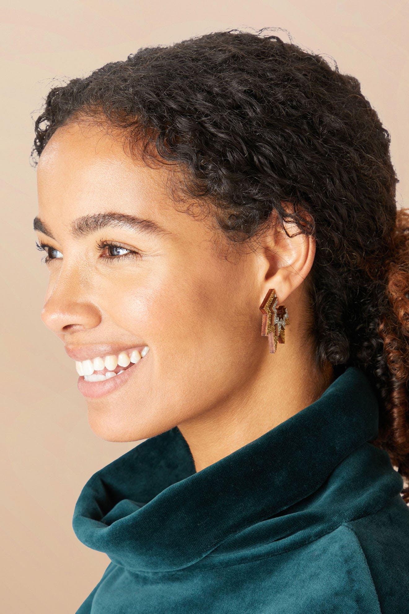 A woman with curly hair and a green velvet top smiles, showcasing her Mini Laser Cut Sparkle Hoops.