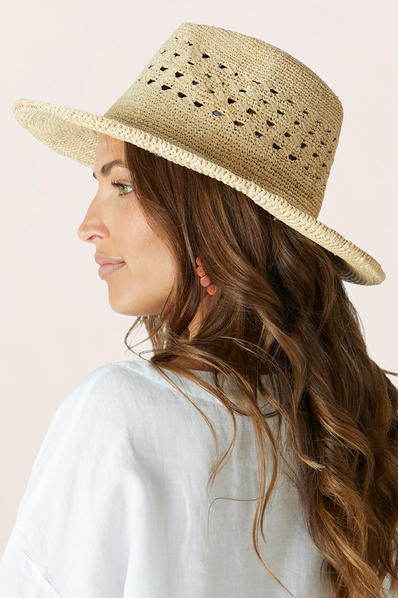 A woman with long brown hair is seen from the side wearing the Chapeau Westosia, a close weave lightweight summer hat, paired with a light-colored top against a plain background.