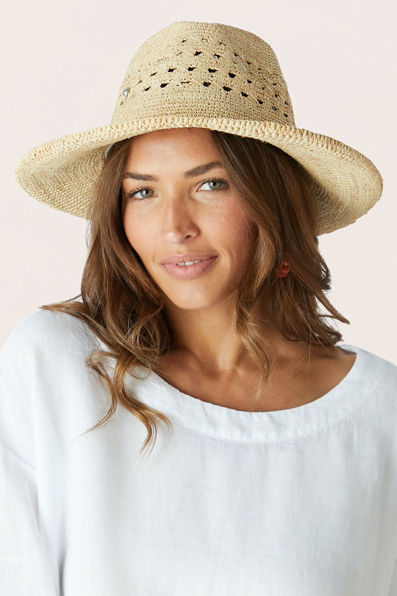 Woman wearing the Chapeau Westosia, a close weave hat, and a loose white top, gazing at the camera with a neutral expression.