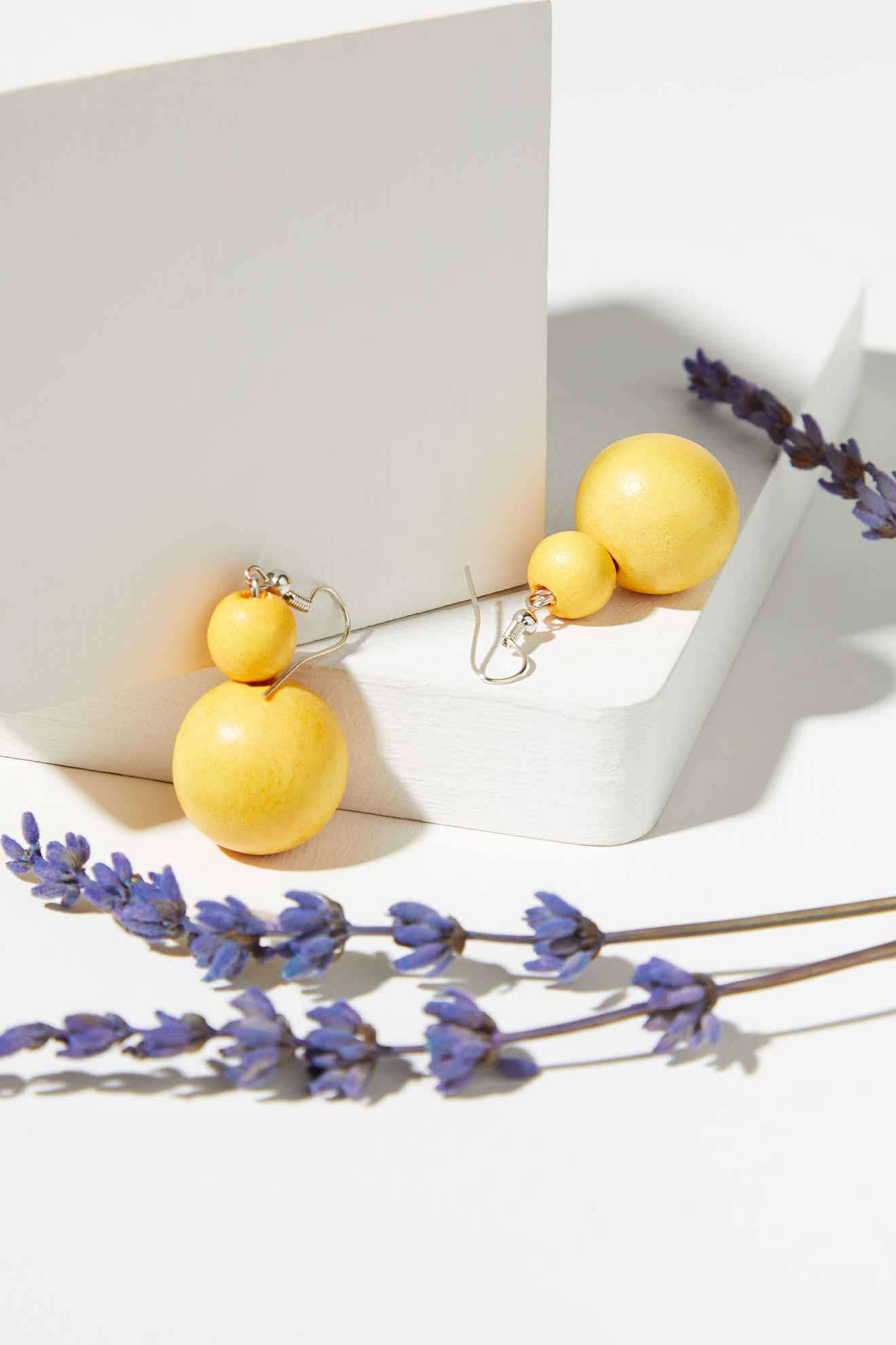 A pair of Double Sphere Earrings adorned with wooden beads on a white table next to lavender.