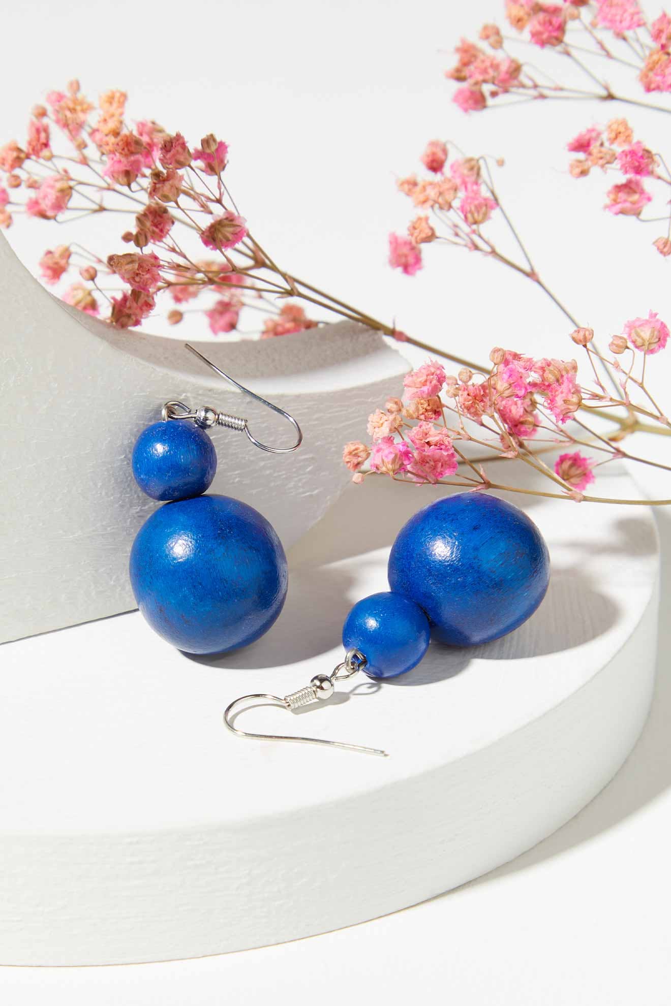 A pair of Double Sphere Earrings, decorated with wooden beads, sitting on a white surface.