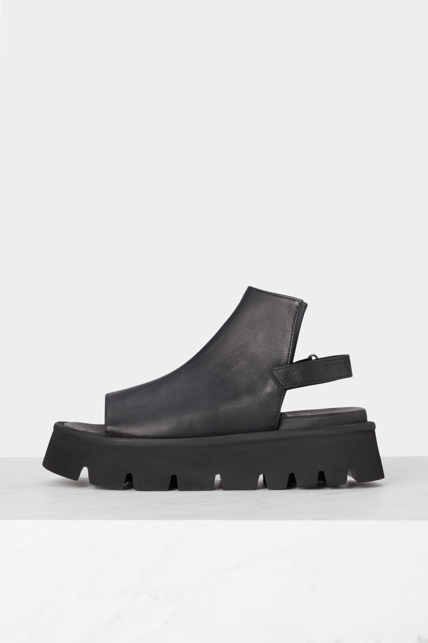 A pair of Buckle Back Sandals - minimalist style leather sandals on a marble floor.