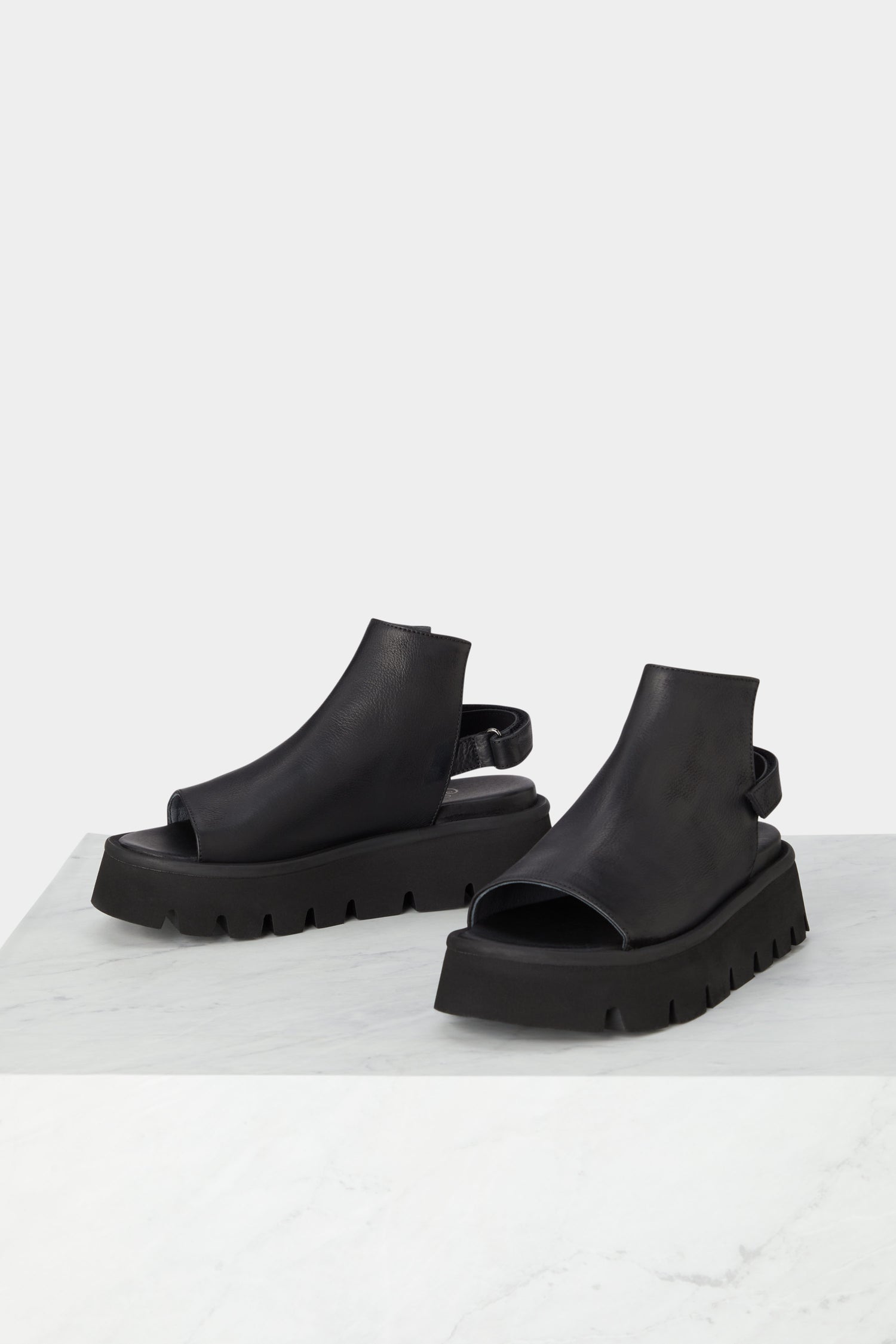 A pair of Buckle Back Sandals on a minimalist style marble table.