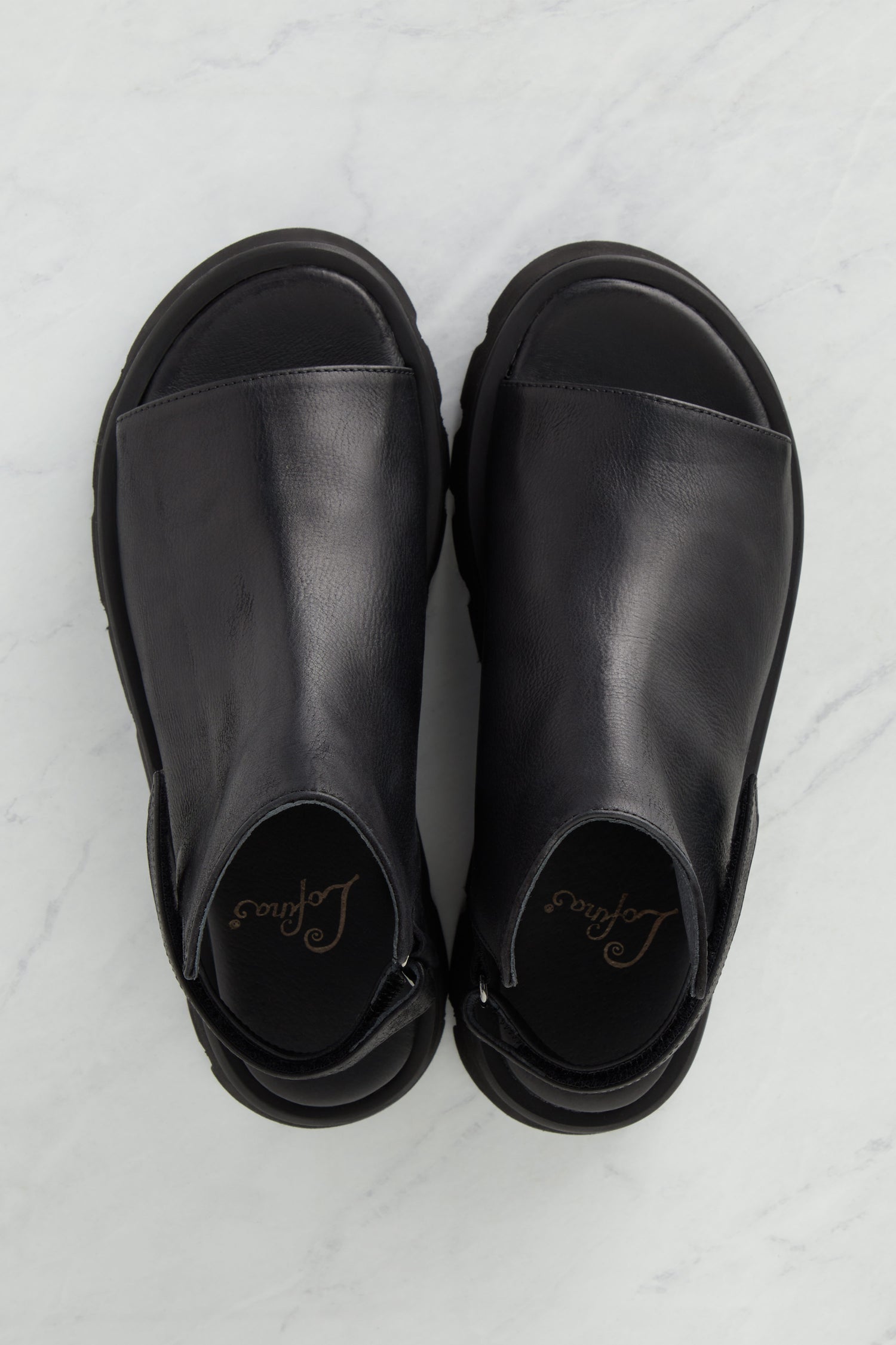 A pair of Buckle Back Sandals with a minimalist style on a marble surface.