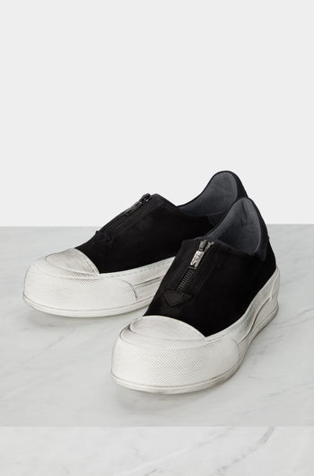 A pair of black slip on Zip Detail Suede Pumps, with a minimalist style, on a marble floor.