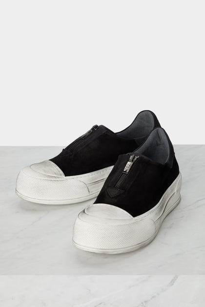 A pair of black slip on Zip Detail Suede Pumps, with a minimalist style, on a marble floor.