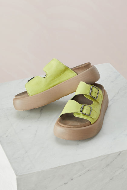 A pair of Lime Leather Flatform Sandal yellow sandals on a marble table.