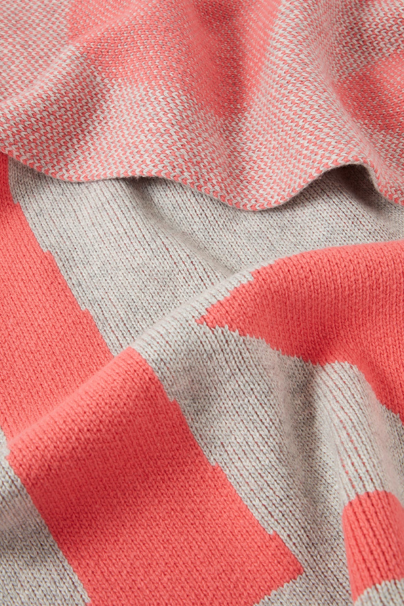 Close-up of the Recycled Wool Allsorts Scarf, featuring pink and gray knit patterns with delicate houndstooth and bold geometric designs. This sustainable knitwear is draped and layered, highlighting the intricate craftsmanship from a family-run factory.