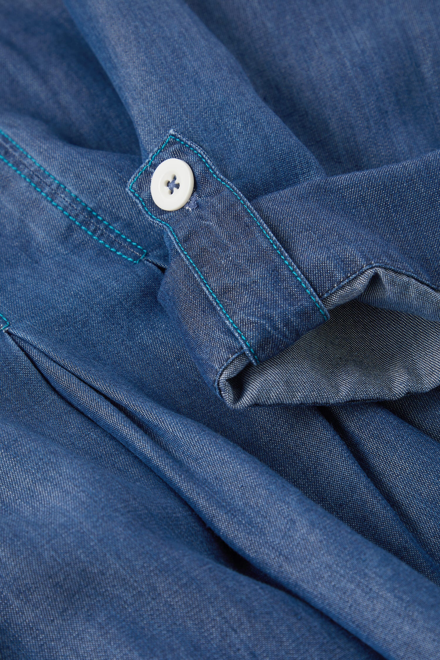 Close-up of a Fluid Denim Relaxed Shirt focusing on the cuff with a white button and contrasting blue stitching.