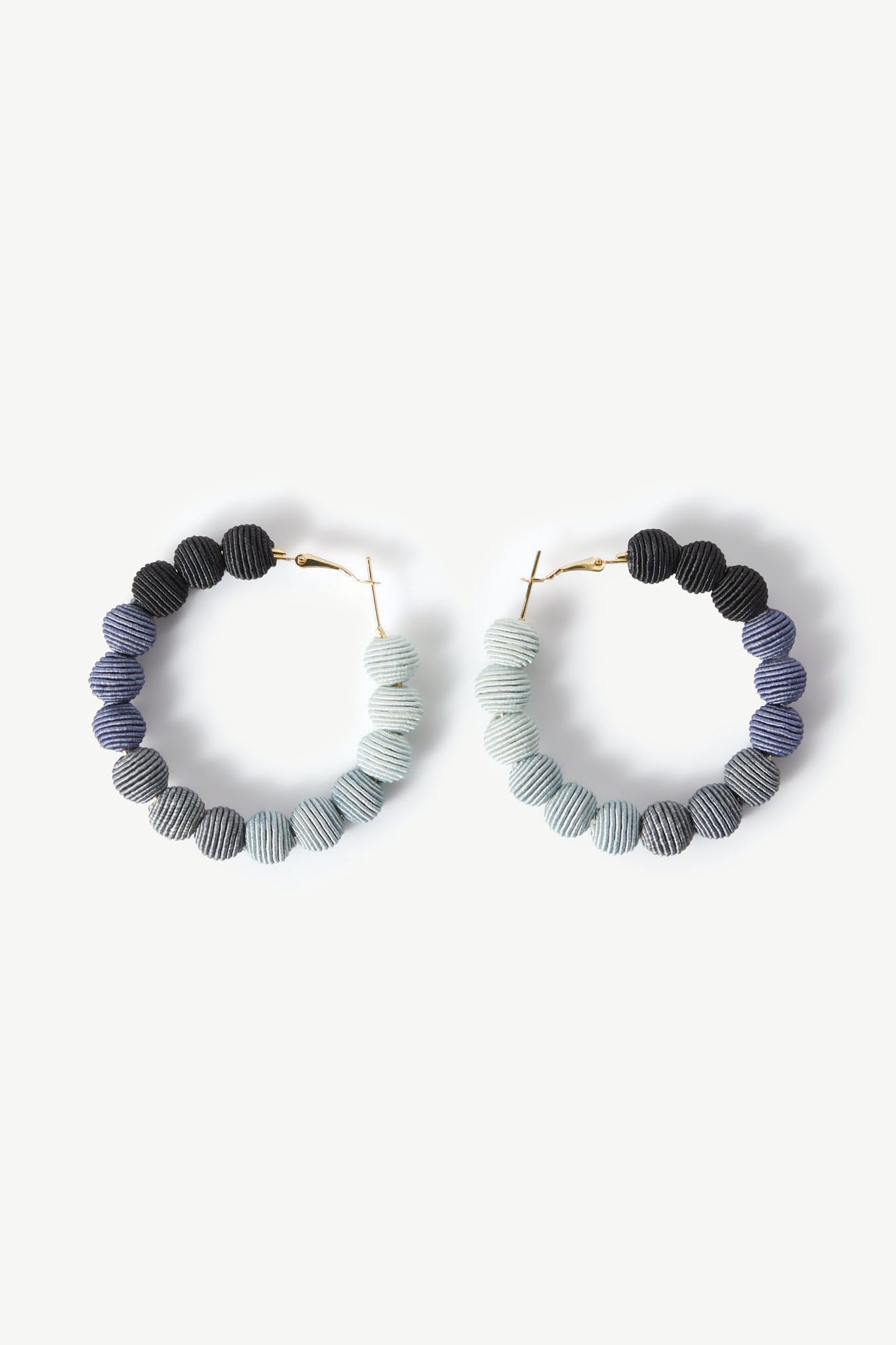 The Woven Ball Hoop earrings feature a circular design with gradient colored beads transitioning from dark blue to light gray, arranged on a white background, showcasing a subtle bohemian style.