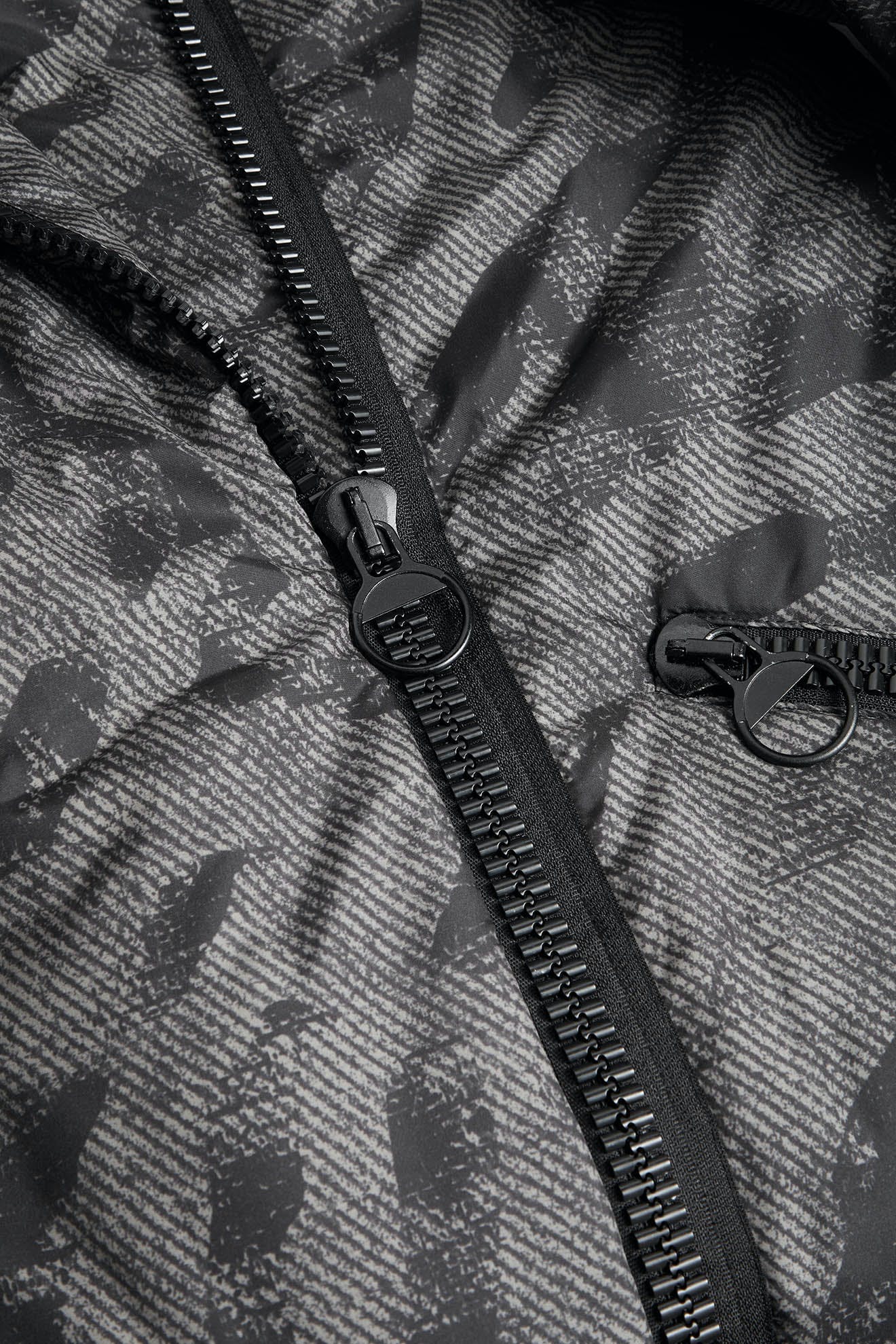 Close-up of the Zip Print Coat, a black puffer jacket with a textured pattern, featuring a partially open zipper and visible zipper teeth.