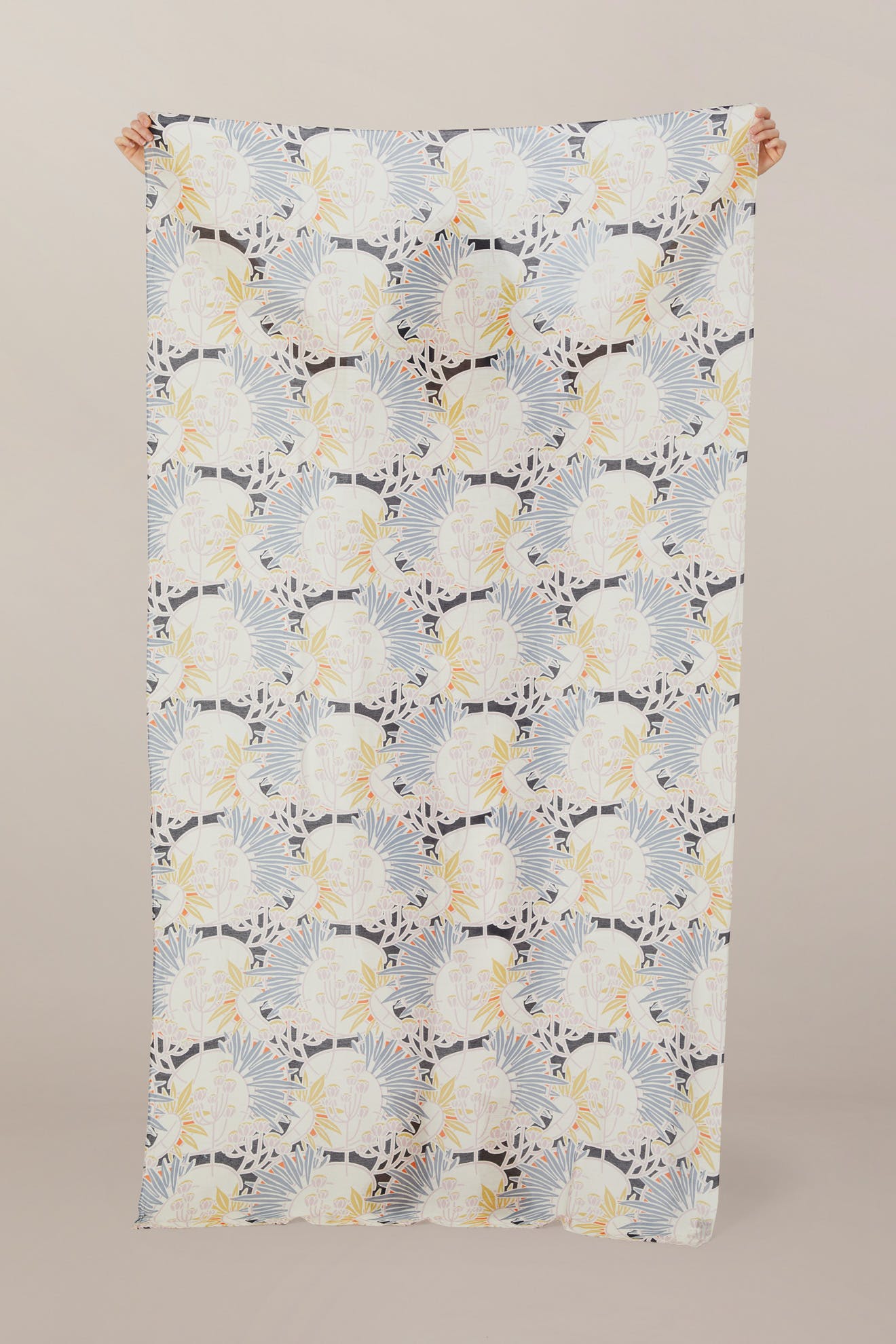 A person holds up the Deco Daisy Scarf, a rectangular modal viscose fabric featuring a blue, yellow, and black abstract leaf pattern reminiscent of botanical artistry, against a plain background.