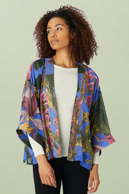A woman with a calm expression wears the Kew Magnolia Kimono, a floral design crafted from lightweight modal viscose, over a white top.