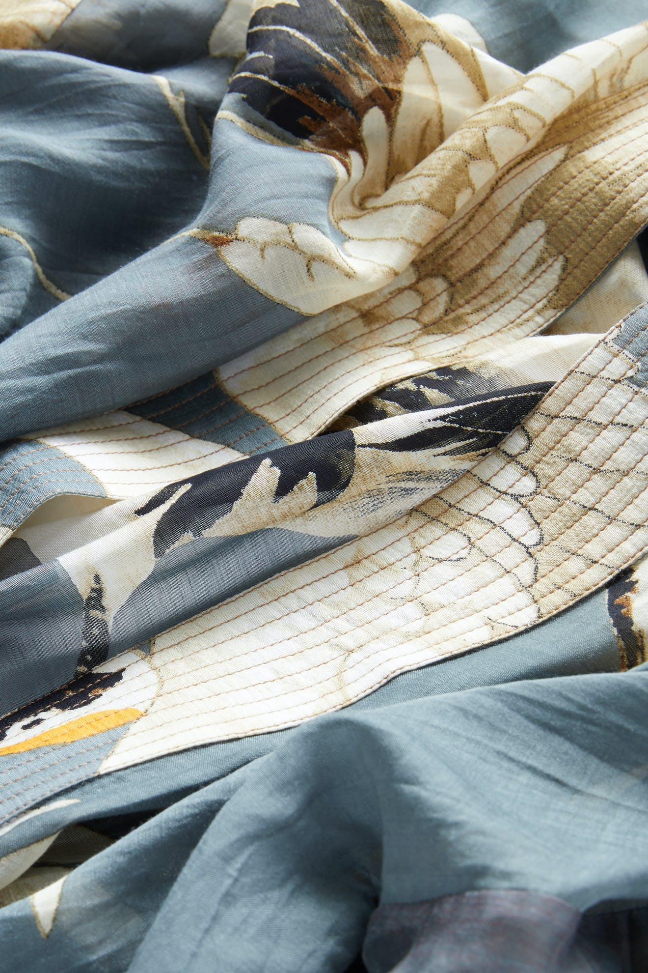 A close-up of the Stork Kimono reveals blue and beige fabric adorned with a feather pattern, expertly crafted in lightweight modal viscose, showcasing soft folds and intricate detailing.