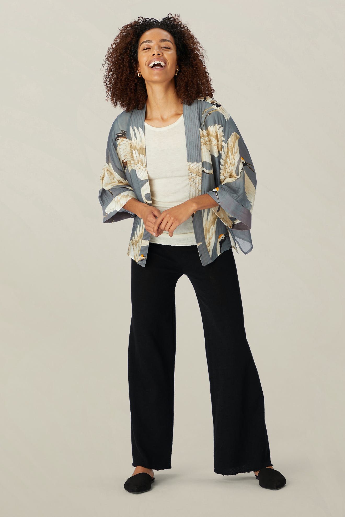 A person wearing the Stork Kimono from the Kew Gardens collaboration, combined with a lightweight modal viscose white top, black pants, and black shoes, stands against a plain background.