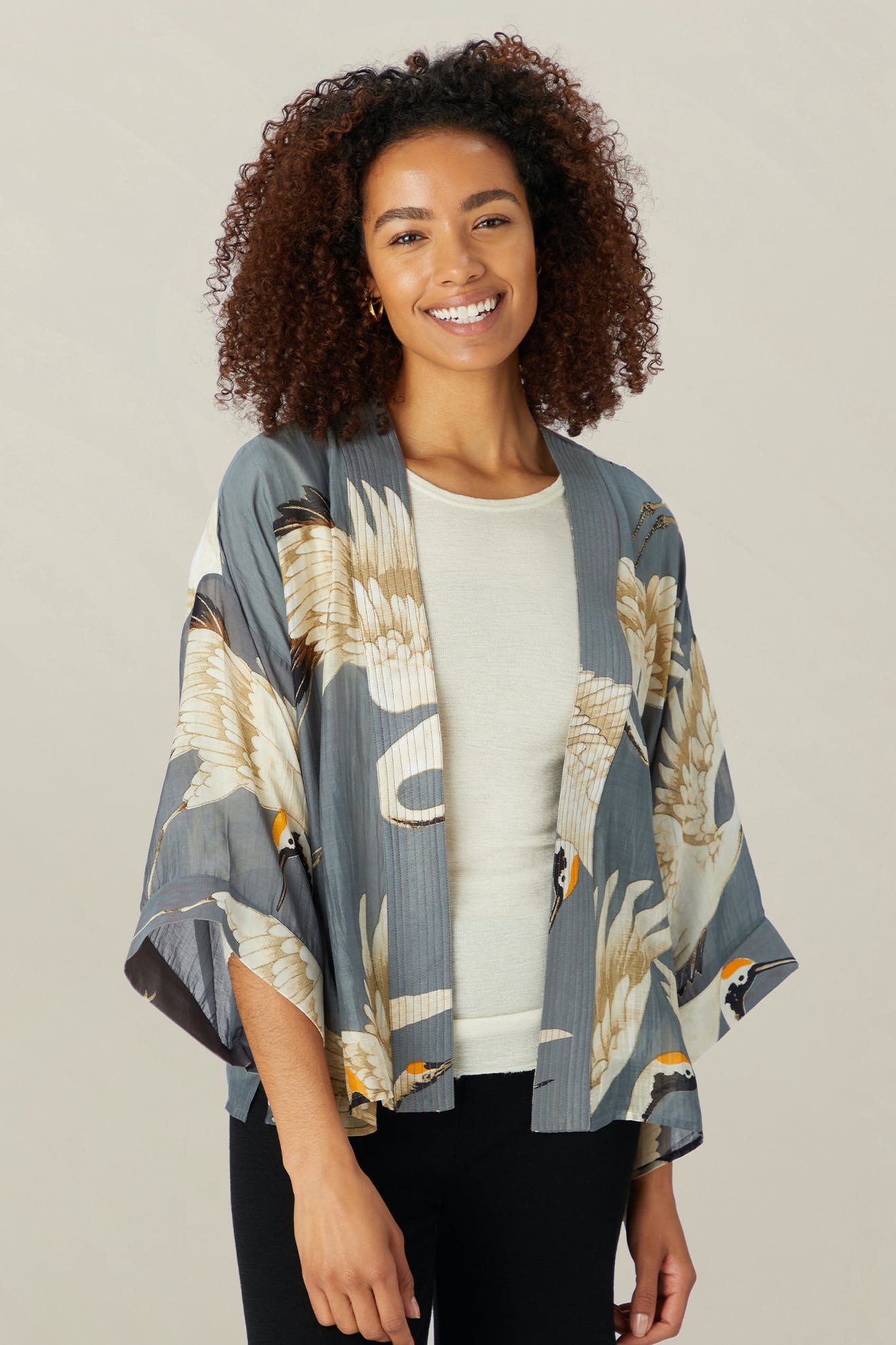 A person smiles while wearing the Stork Kimono, crafted from lightweight modal viscose, over a white shirt, standing against a plain background.