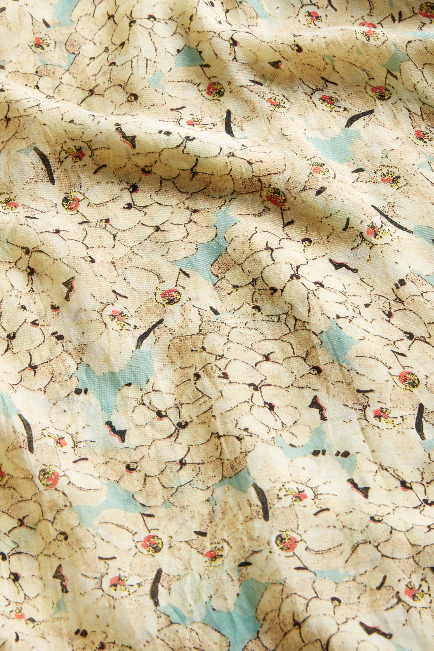 Close-up of the Blossom Blue Throwover by One Hundred Stars, featuring a cream and beige floral design with light blue, pink, and yellow accents. The lightweight fabric has a slightly wrinkled texture.