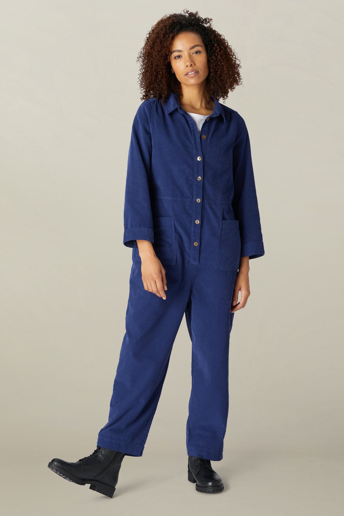 Woman in a long sleeve blue Cotton Babycord Jumpsuit standing against a neutral background, posing with one hand in pocket.