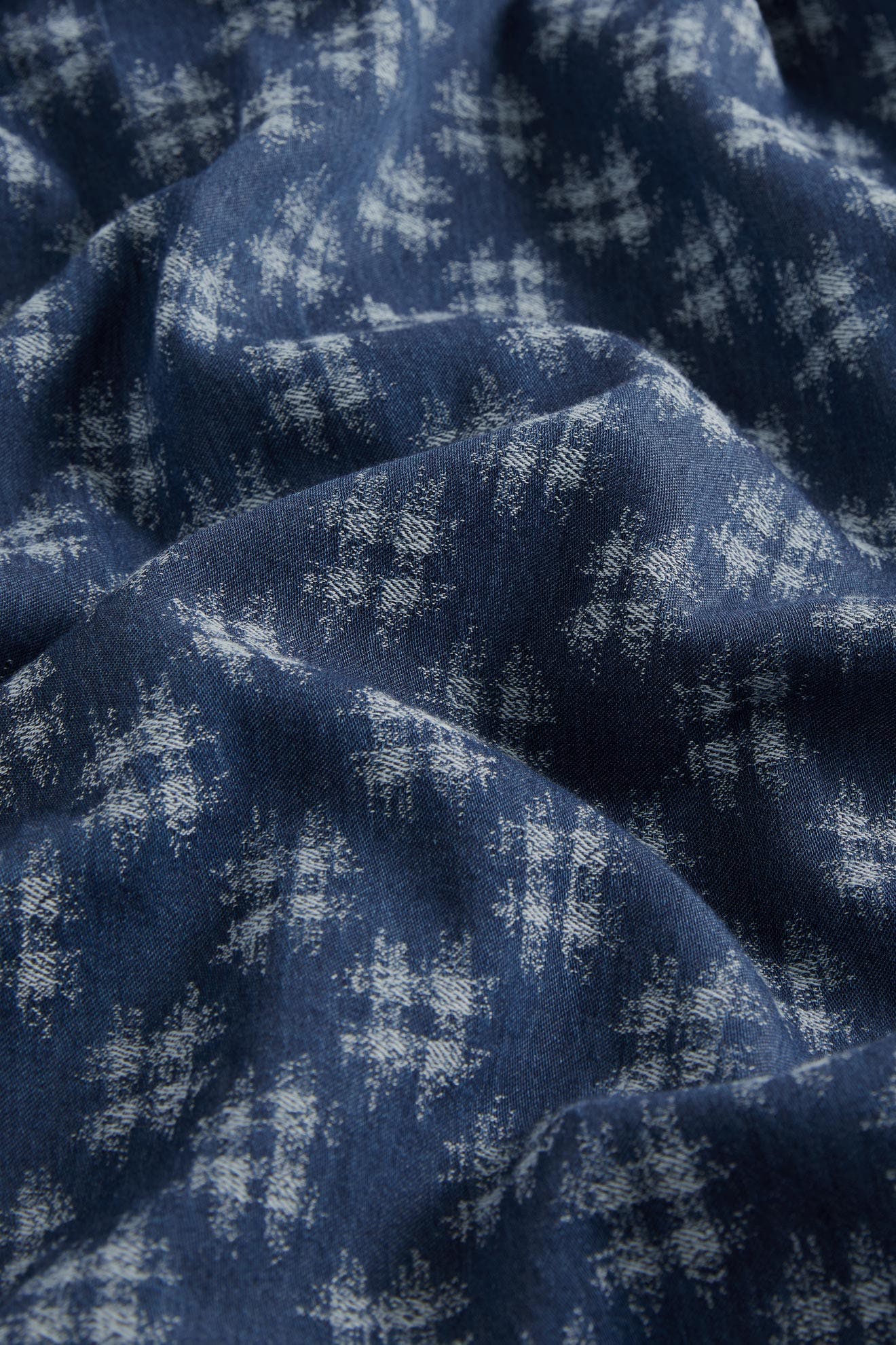 Close-up of a Broken Check Denim Jumpsuit with a subtle, white snowflake pattern, highlighting the texture and folds of the material.