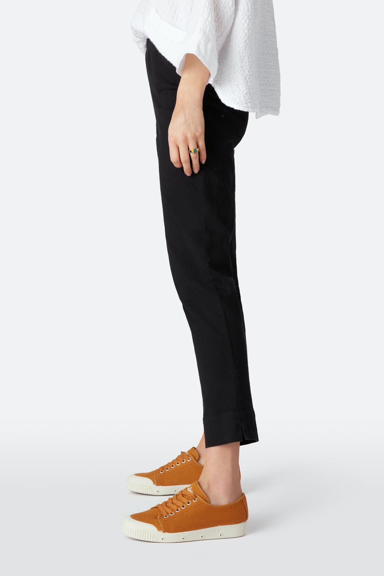 A person stands sideways wearing black Stretch Cotton Twill Trouser with an elasticated waist, a white textured top, and orange low-top sneakers with white soles.